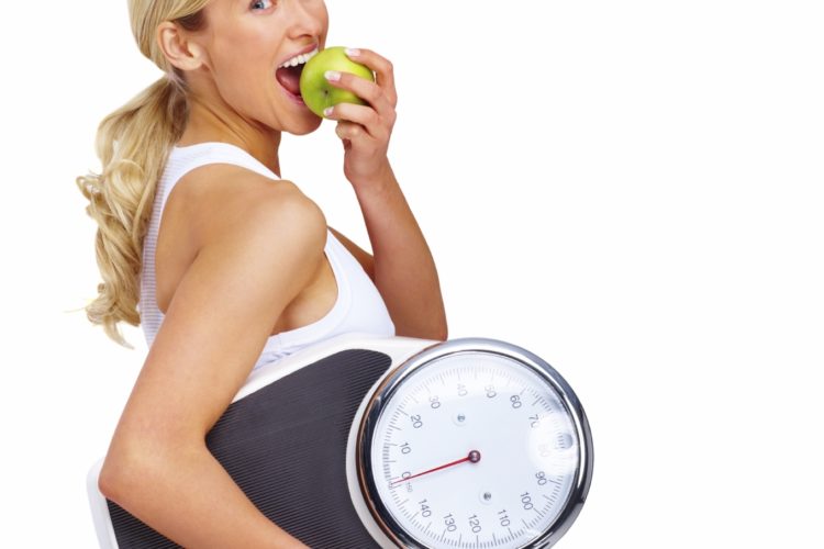 Young woman eating apple and carrying a weight scale over white background Young woman eating apple and carrying a weight scale over white background